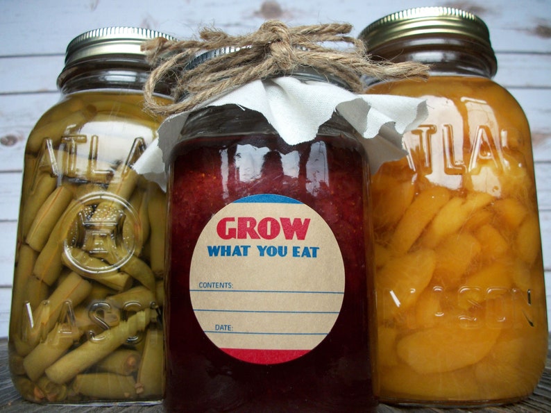 May include: Three glass jars with lids, filled with preserved foods. The center jar has a red and blue circular label that reads "Grow What You Eat".