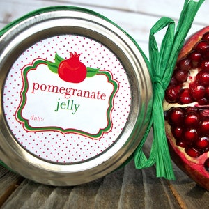 May include: A white jar with a red and green polka dot label that says "pomegranate jelly" and "date:". The jar is next to a half of a pomegranate.