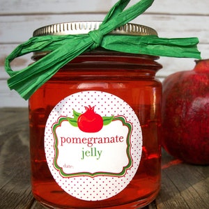 May include: A glass jar filled with red pomegranate jelly, topped with a green ribbon bow. The jar has a white label with red polka dots and the text "pomegranate jelly" and "date:".