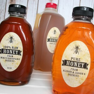 Vintage looking oval honey labels on the front of honey bottles filled with honey. Label art has a realistic honey bee up top with printed text for pure honey.