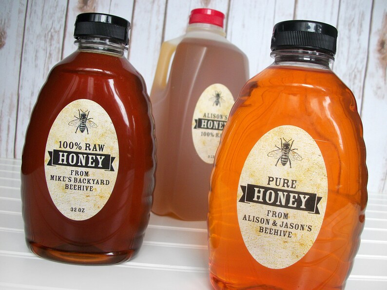 Vintage looking oval honey labels on the front of honey bottles filled with honey. Label art has a realistic honey bee up top with printed text for pure honey.