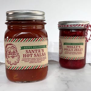 Peut inclure: Deux bocaux en verre de produits alimentaires de vacances. L'un est étiqueté "Santa's Hot Salsa" avec un dessin du Père Noël et une liste d'ingrédients. L'autre est étiqueté "Molly's Jolly Jelly" sur le thème de Noël.