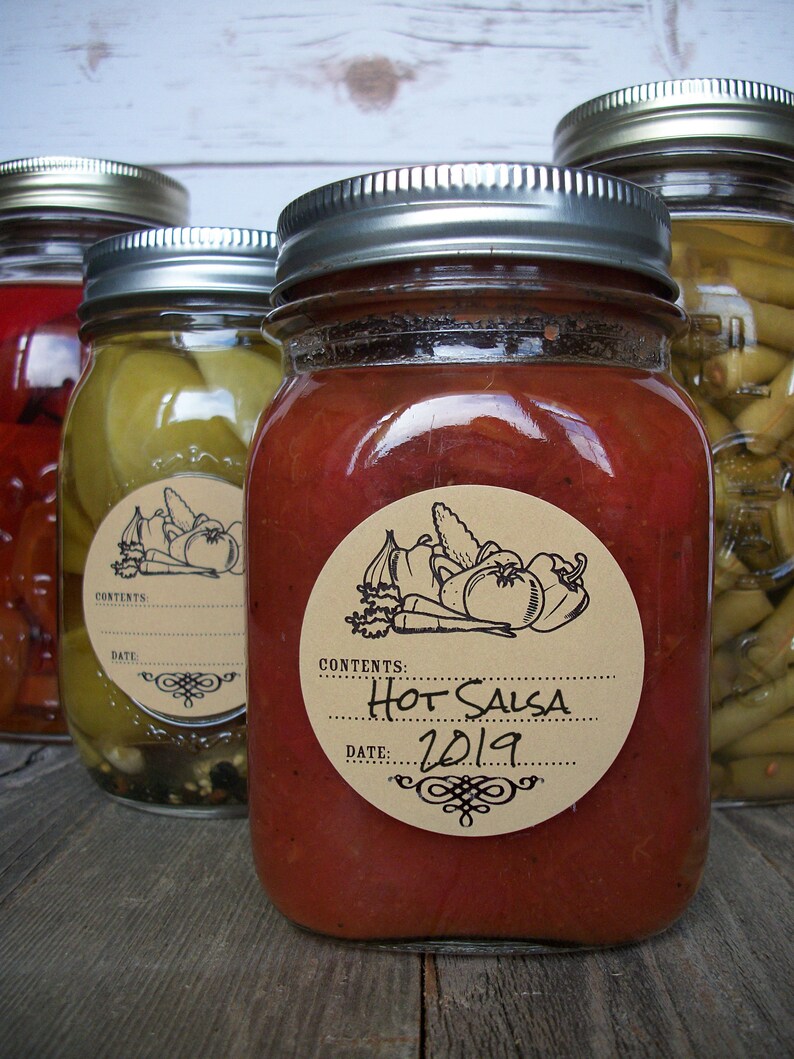 May include: Three glass jars with silver lids and brown paper labels. The jars contain red salsa, green beans, and red peppers. The labels have the words "Contents: Hot Salsa Date: 2019" printed on them.