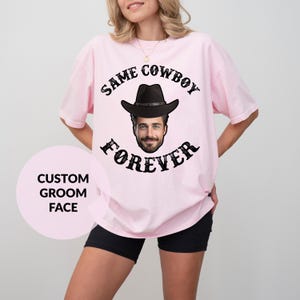 May include: Pink t-shirt with the text "Same Cowboy Forever" in black with a custom groom face in a cowboy hat.