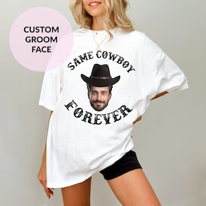 May include: White t-shirt with a black cowboy hat and face graphic. The text "SAME COWBOY FOREVER" is printed on the shirt.