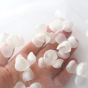 May include: White fabric flower petals on a white mesh background. The petals are arranged in a cluster and are slightly overlapping.