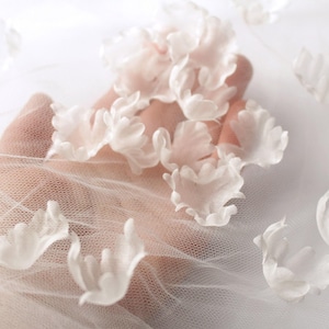 Peut inclure: Tissu de dentelle blanche avec de délicates fleurs en 3D. Le tissu est transparent et a une sensation douce et romantique.