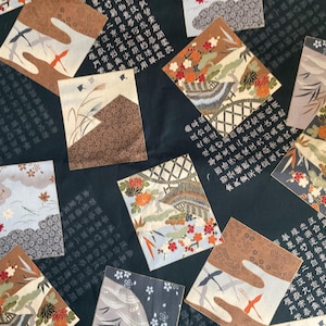 May include: A dark teal fabric with a repeating pattern of square panels. Each panel features a different Japanese-inspired design, including landscapes, birds, and floral motifs in shades of brown, orange, and blue. The background is filled with Japanese characters.