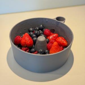 Könnte beinhalten: Eine graue Obstschale aus Beton, gefüllt mit frischen Erdbeeren, Blaubeeren und Himbeeren. Die Schale hat einen zentralen Kegel und einen Griff. Der Text "Washy: Concrete" ist sichtbar.