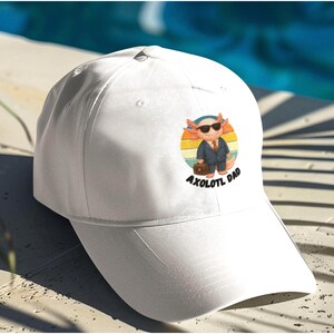 May include: White baseball cap featuring a cartoon axolotl wearing sunglasses and a suit, carrying a briefcase. The axolotl is set against a retro sunset design, with the text "AXOLOTL DAD" below.