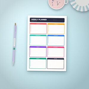 Peut inclure: Une feuille de planning hebdomadaire avec un en-tête sombre portant l'inscription WEEKLY PLANNER, comprenant sept sections rectangulaires colorées pour chaque jour avec des lignes de liste, une section notes et un stylo violet clair à gauche.