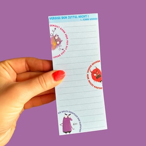 Könnte beinhalten: Ein liniertes Notizblock mit dem Text "VERGISS DEN ZETTEL NICHT!" in Blau. Der Notizblock zeigt Cartoon-Illustrationen von Monstern und humorvollen Sätzen auf Deutsch, wie "Gemüse? Dann aber nur mit Käse drauf!" und "Weniger denken, mehr Snacks kaufen!"