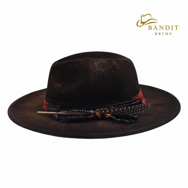May include: A brown fedora hat with a wide brim, adorned with a black band, red accents, and decorative feathers. The hat has a distressed finish, giving it a vintage look. The hat is a stylish accessory.