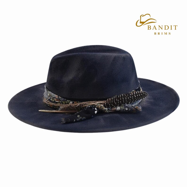May include: A navy blue fedora hat with a wide brim, adorned with a patterned band and decorative feathers. The hat features the "Bandit Brims" logo in gold. This stylish hat is a fashion accessory.