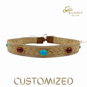 May include: A beige choker necklace with woven detailing, featuring three oval gemstones in gold settings. The gemstones are red and turquoise. The text "CUSTOMIZED" is at the bottom, and the brand logo "BANDIT BRIMS" is at the top.
