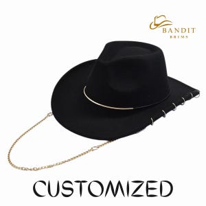 May include: A black fedora-style hat with a gold-coloured band and chain. The hat has a wide brim and is adorned with small silver rings. The word "CUSTOMIZED" is printed in black below the hat.