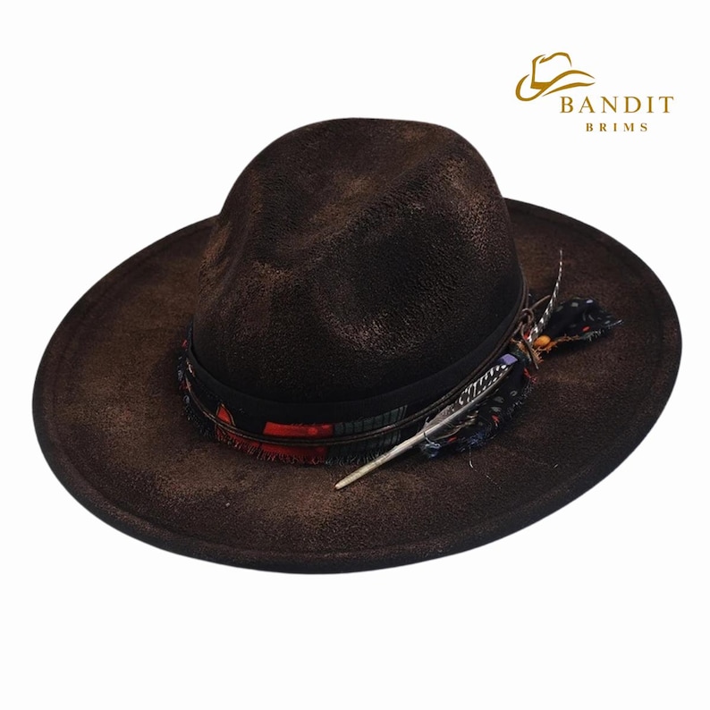 May include: A brown fedora-style hat with a wide brim. The hat features a black band with colorful accents and a decorative feather. The hat has the text "BANDIT BRIMS" in gold.
