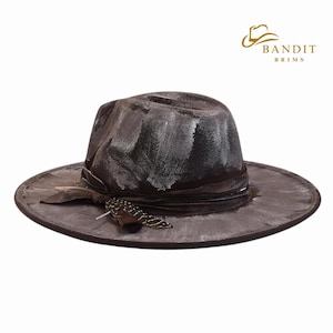 May include: A distressed brown fedora-style hat with a wide brim. The hat features white paint strokes and a dark brown band with a decorative feather. The hat has the text "BANDIT BRIMS" in gold.
