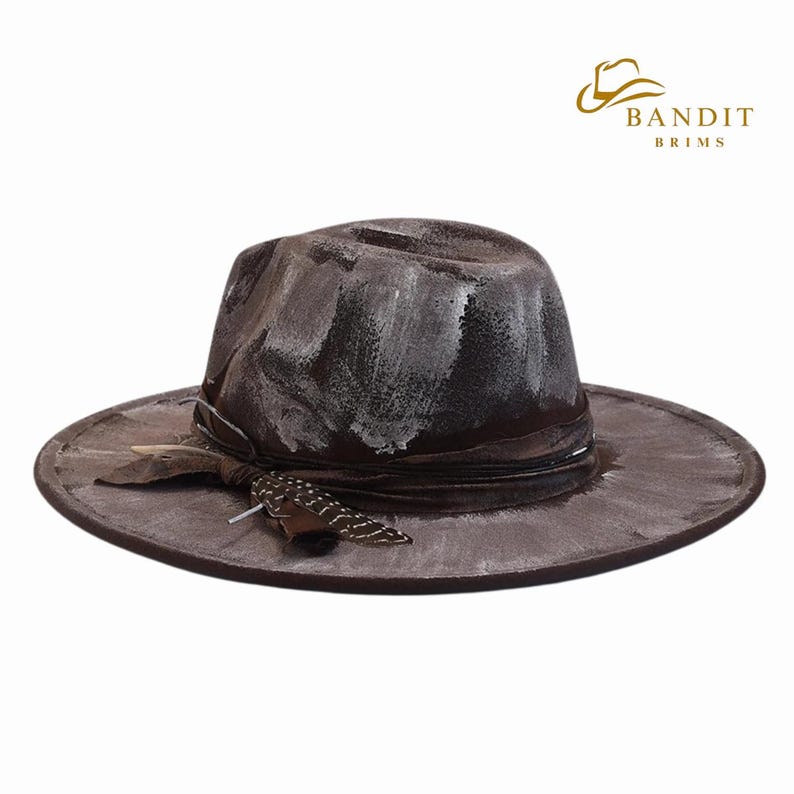 May include: A distressed brown fedora-style hat with a wide brim. The hat features white paint strokes and a dark brown band with a decorative feather. The hat has the text "BANDIT BRIMS" in gold.