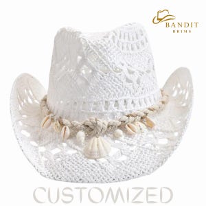 Op de afbeelding: Een witte gehaakte cowboyhoed met een decoratieve touwband en schelpen. De hoed heeft een brede rand en een open ontwerp. Het woord "CUSTOMIZED" staat onderaan afgedrukt. De hoed is van Bandit Brims.