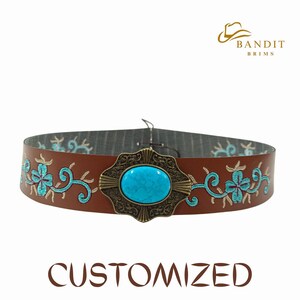 May include: A brown leather belt featuring turquoise floral embroidery and a central turquoise stone. The belt has a decorative metal buckle. The word "CUSTOMIZED" is printed at the bottom.