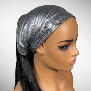 May include: A silver-colored head covering with a fine, textured, shimmering surface. The fabric is fitted closely to the head, featuring a dense, reflective pattern that catches the light, creating a metallic appearance across the entire surface.