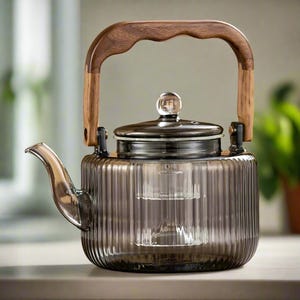 Op de afbeelding: Een glazen theepot met een houten handvat en een ingebouwde zeef. De theepot is helder met een donkergrijze tint en heeft een geribbeld ontwerp.
