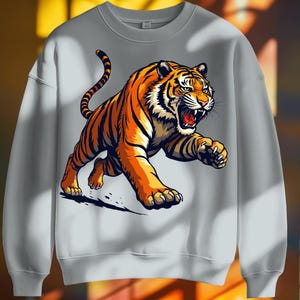 May include: A light gray sweatshirt featuring a detailed illustration of an orange and black tiger in a running pose. The tiger has its mouth open, revealing its teeth and tongue. The design is centered on the front of the sweatshirt.
