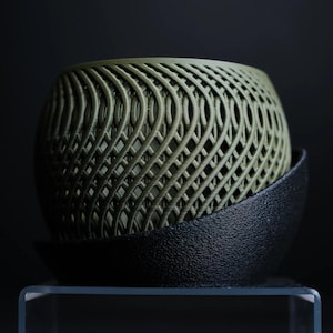 May include: A green geometric planter with a black base. The planter is made of a woven material and has a unique, modern design.