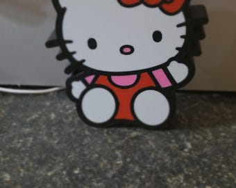 Pode incluir: Uma figura Hello Kitty em preto e branco com um laço vermelho, detalhes em rosa e um vestido vermelho. A figura tem um rosto branco e olhos pretos grandes. A figura está sobre uma superfície escura e texturizada.