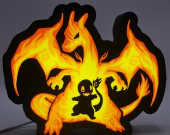Pode incluir: Uma placa luminosa preta e laranja com um design estilizado de Charizard e Charmander. O Charizard é retratado com chamas laranja, e o Charmander é uma silhueta preta. A placa tem uma borda preta e um cabo de alimentação branco.