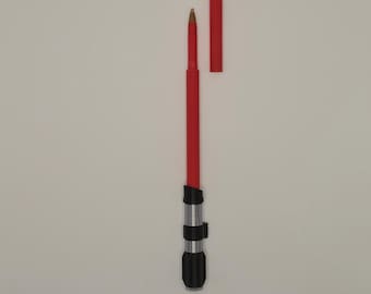 Pode incluir: Uma caneta vermelha com uma pega preta e prateada e uma tampa removível. A caneta foi concebida para se assemelhar a um sabre de luz. A caneta está sobre um fundo branco.