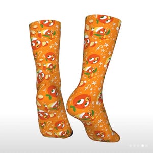 May include: A pair of orange socks with a repeating pattern of cartoon oranges, slices, and stars. The socks are knee-high and have a bright, cheerful design. The background is a solid orange color.