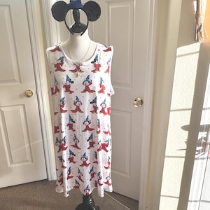 May include: White sleeveless dress with a repeating pattern of a cartoon character in a wizard hat and red robe. A black Mickey Mouse ear headband and a wizard hat are on display. The dress is on a black dress form.