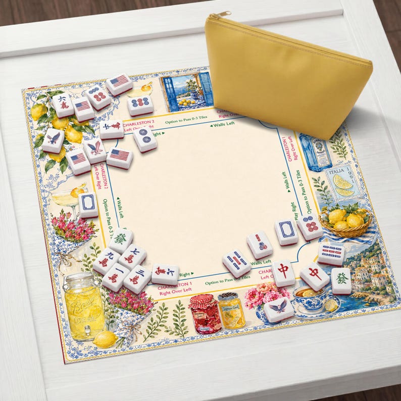 May include: A mahjong set with tiles, a decorative mat, and a yellow zippered pouch. The mat features a floral and lemon design with text. The tiles have various symbols and markings. The set is on a white surface.