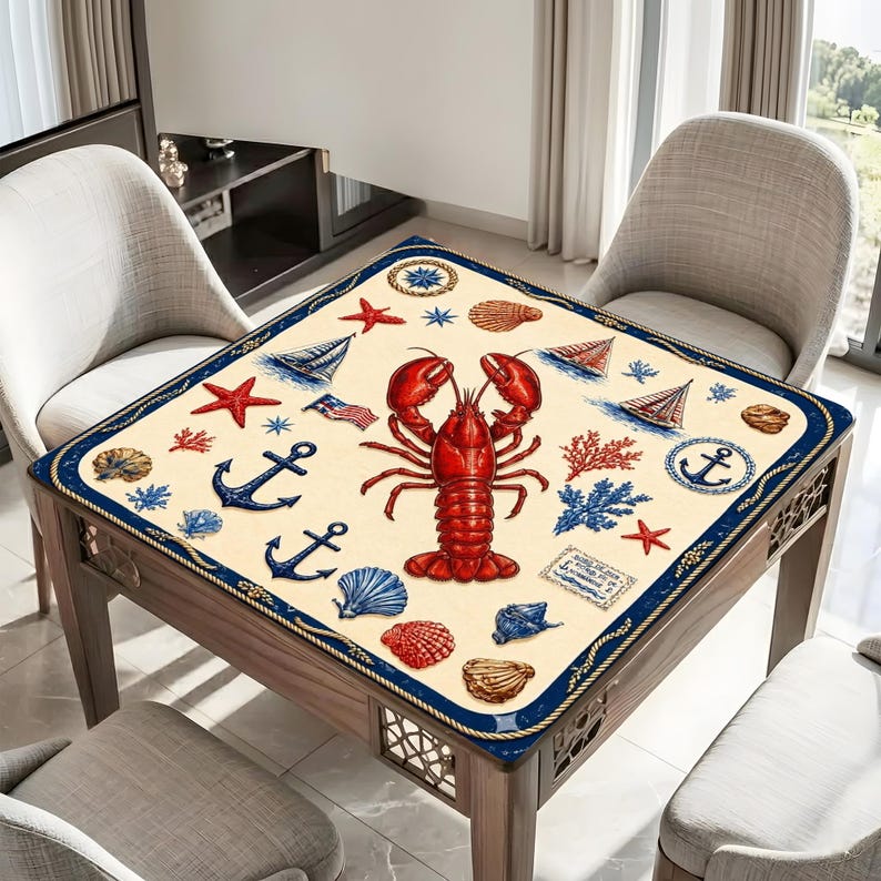 May include: Square table cover with a nautical theme. The cream-colored cover features a large red lobster, anchors, sailboats, seashells, and starfish. A navy blue rope border frames the design.