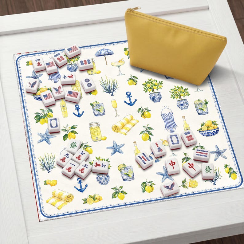 Puede incluir: Una bolsa amarilla con cremallera descansa sobre una alfombra decorativa con tem&aacute;tica n&aacute;utica. La alfombra presenta ilustraciones de limones, c&oacute;cteles y anclas, junto con varias fichas de mahjong. Las fichas tienen marcas rojas y blancas.