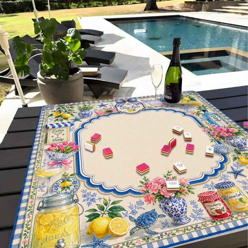 Puede incluir: Un tablero de juego decorativo con un dise&ntilde;o floral y n&aacute;utico, con limones, tarros y una tortuga. Las piezas del juego rosas y blancas est&aacute;n esparcidas por el tablero. Una botella de champ&aacute;n y una copa est&aacute;n sobre la mesa.
