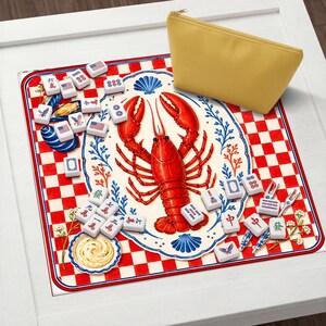 Op de afbeelding: Een rood-wit geblokte Mahjong-speelmat met een centrale illustratie van een rode kreeft. De mat is omgeven door Mahjong-tegels en een gele etui met ritssluiting.