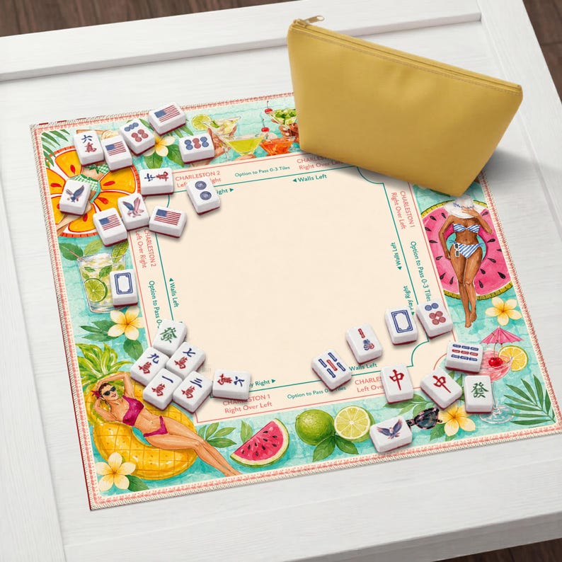 Op de afbeelding: Een Mahjong-set met tegels met verschillende symbolen en Amerikaanse vlagontwerpen, gerangschikt op een kleurrijke mat met tropische illustraties. Een gele etui met ritssluiting ligt rechtsboven. De mat heeft illustraties van cocktails, fruit en vrouwen in badkleding.