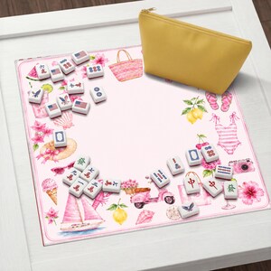 Puede incluir: Un tapete de mahjong cuadrado con fondo rosa claro que presenta ilustraciones en acuarela de art&iacute;culos de verano como un velero, un scooter y un helado, acompa&ntilde;ado de fichas de mahjong dispersas y un estuche amarillo liso.