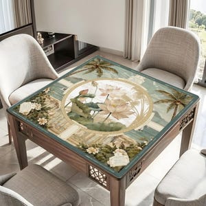 May include: A square table mat featuring a central circular medallion with light pink lotus flowers and green leaves. The background displays a tropical landscape with palm trees, white flowers, and a Greek key border. Text reads DRACYS COLLECTION.