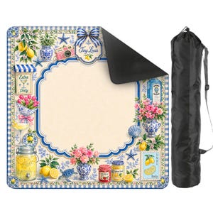 Puede incluir: Una manta de picnic decorativa con un borde azul y blanco, con limones, flores y tarros de conservas. La manta tiene un &aacute;rea central de color crema y una bolsa de transporte negra.
