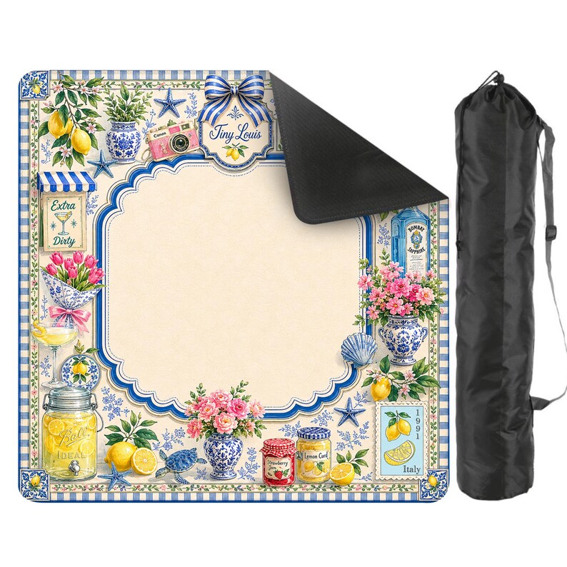 Puede incluir: Una manta de picnic decorativa con un borde azul y blanco, con limones, flores y tarros de conservas. La manta tiene un &aacute;rea central de color crema y una bolsa de transporte negra.