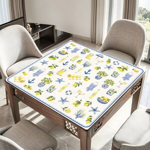 Puede incluir: Una mesa cuadrada con un mantel decorativo con un estampado n&aacute;utico y de c&iacute;tricos. El dise&ntilde;o incluye limones, estrellas de mar, anclas y camisas a rayas azules y amarillas. La mesa est&aacute; rodeada de sillas.