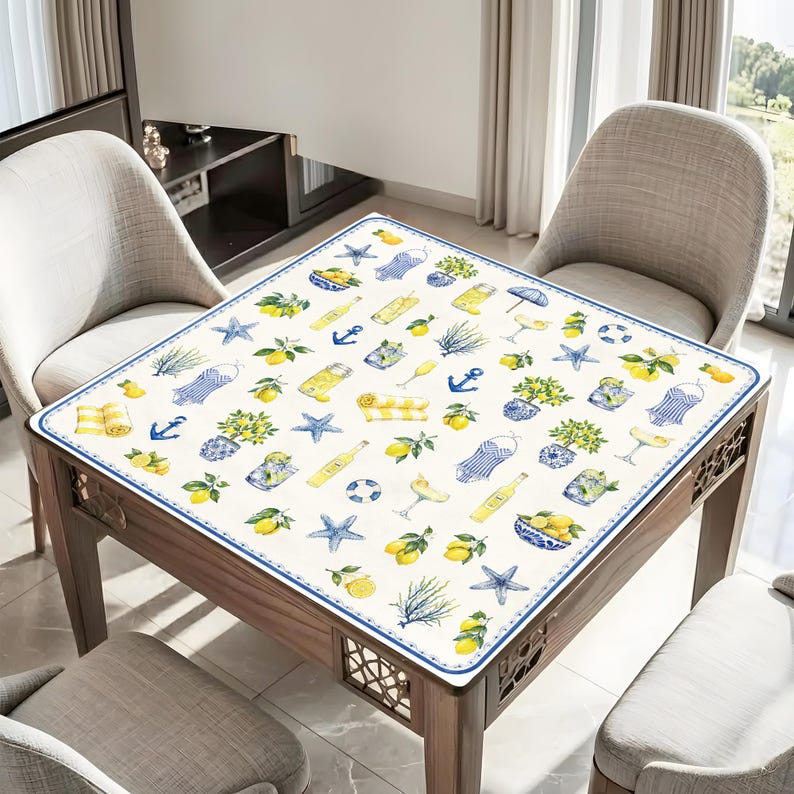 Puede incluir: Una mesa cuadrada con un mantel decorativo con un estampado n&aacute;utico y de c&iacute;tricos. El dise&ntilde;o incluye limones, estrellas de mar, anclas y camisas a rayas azules y amarillas. La mesa est&aacute; rodeada de sillas.