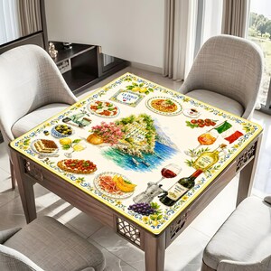 May include: A square tablecloth featuring a vibrant Italian-themed print with illustrations of coastal buildings, pasta dishes, wine, grapes, lemons, and a scooter. The design includes the text LA DOLCE VITA and a decorative blue and yellow border.