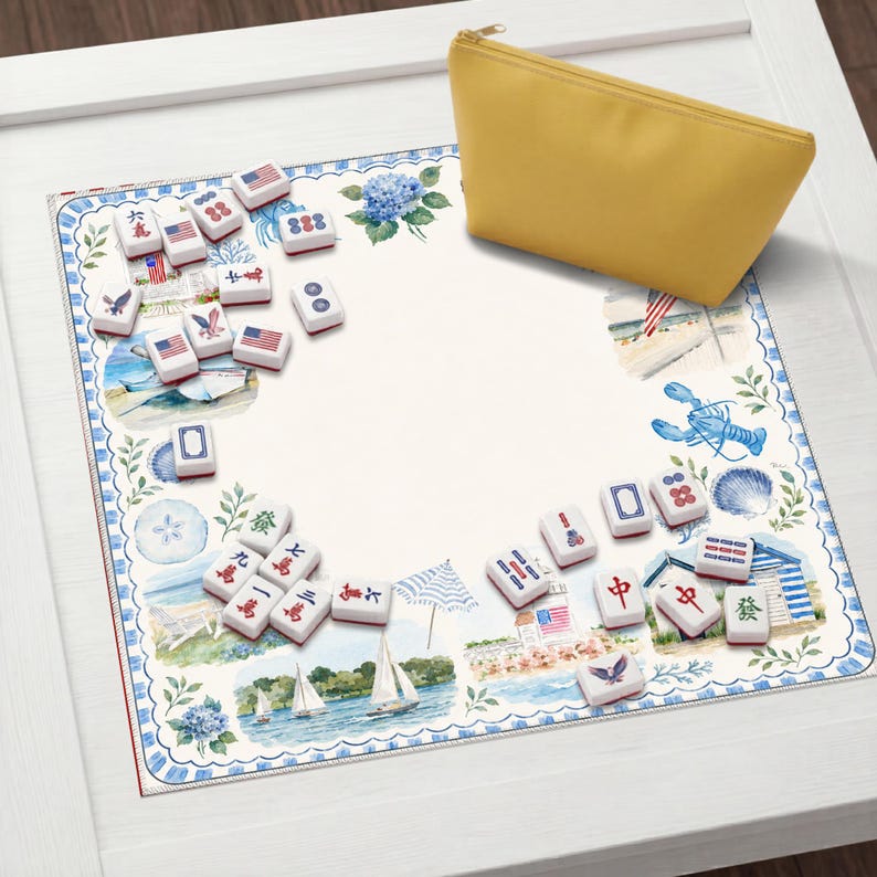 May include: A square mahjong mat featuring a coastal-themed border with illustrations of sailboats, lighthouses, lobsters, and hydrangeas, accompanied by a set of white mahjong tiles with red and blue markings and a solid yellow zippered storage pouch.