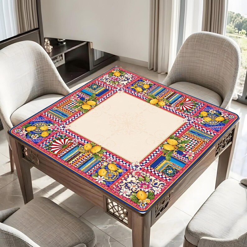 Pode incluir: Mesa quadrada de madeira com um tampo estampado colorido. A borda apresenta desenhos florais, geom&eacute;tricos e de frutas em vermelho, azul, amarelo e branco. A mesa &eacute; cercada por quatro cadeiras cinzentas. Aproximadamente 90 cm x 90 cm.