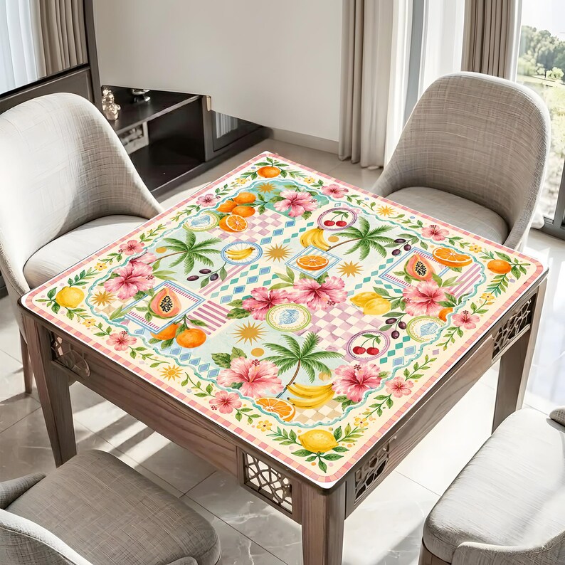 Pu&ograve; includere: Un tavolo quadrato con un colorato design di frutta tropicale e fiori. Il tavolo ha una struttura in legno chiaro e un piano a fantasia con arance, banane, ciliegie e fiori di ibisco. Il tavolo &egrave; circondato da sedie.